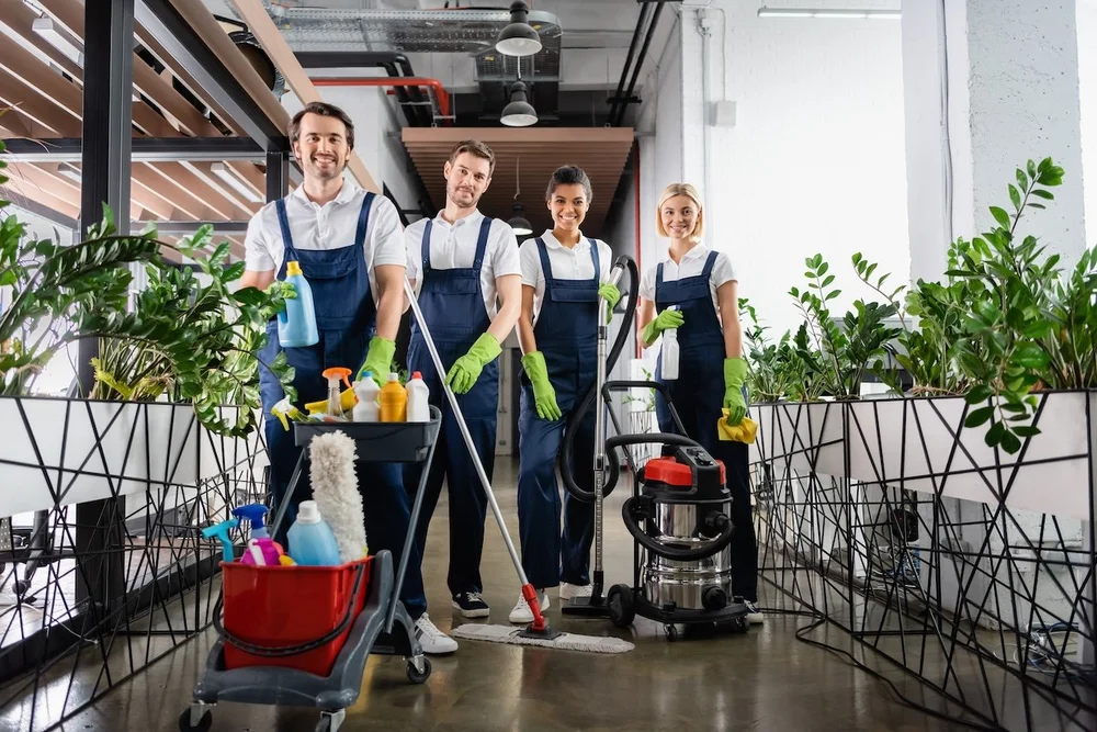 Four uniformed professional cleaners with their equipment in an office