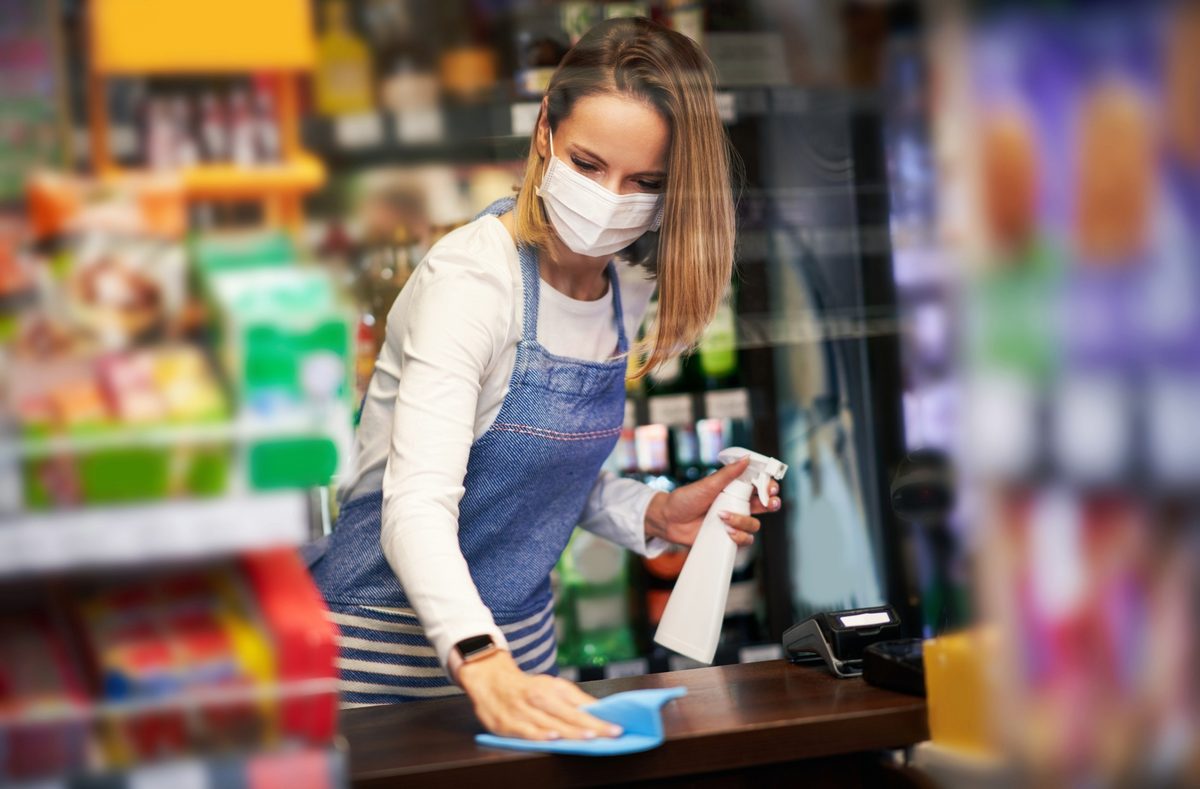 A worker sanitizing a retail store checkout counter